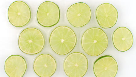 a lot of lime slices lie on white in the background in slow motion falling water splashes.