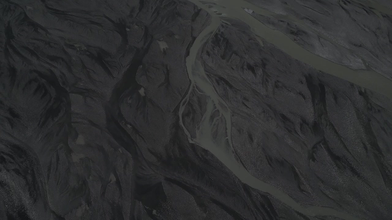 Vuelo de dron aéreo sobre el terreno oscuro y texturizado y el suelo accidentado del valle bajo los Conos de Passu en Pakistán, destino de viaje de aventura.