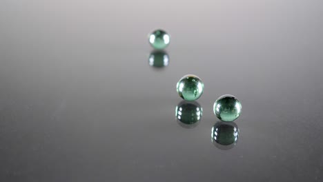 three small emerald green glass balls sliding over a reflective glass in slow motion