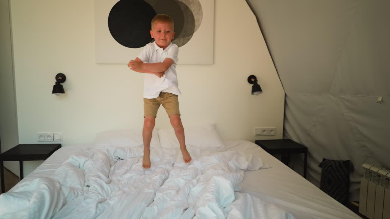 아기 소년은 현대적인 침실에서 밝은 색의 은 침대에 뛰어들고, 남성은 일시적인 비행에서 긍정적인 감정을 얻는 재미를 느니다.