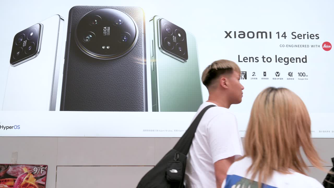 Pedestrians pass by an advertisement for the Xiaomi 14 Series smartphone displayed outside the brand's official flagship store.