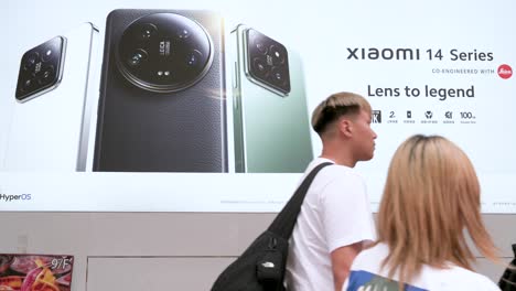 pedestrians pass by an advertisement for the xiaomi 14 series smartphone displayed outside the brand's official flagship store.