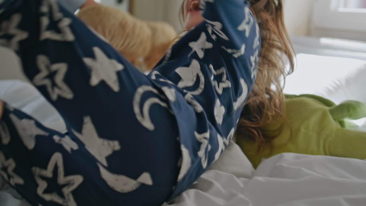 Mom tickling overjoyed toddler at bed closeup. Laughing little girl having fun