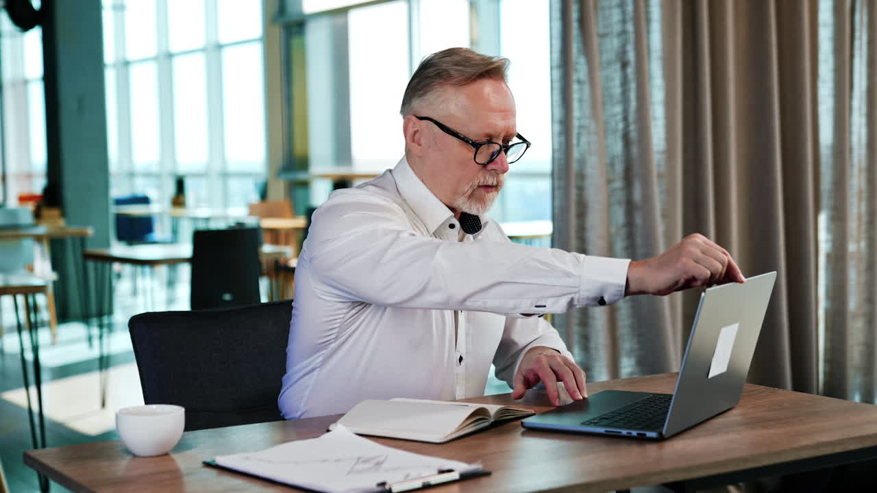Businessman in white shirt sits at desk and opens his laptop. Starting productive workday in the morning.
