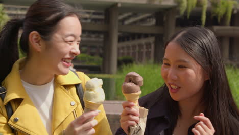 Two-Smiling-Young-Female-Friends-Meeting-And-Eating-Ice-Cream-Outdoors-In-Park-Together-2