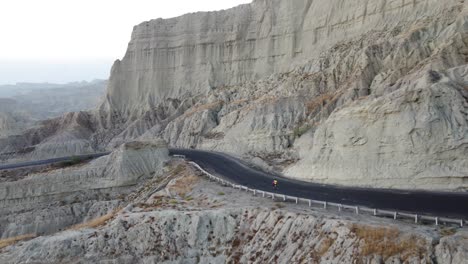 vista aérea de un ciclista montando en una carretera remota al lado de un dramático acantilado rocoso en la carretera costera de makran