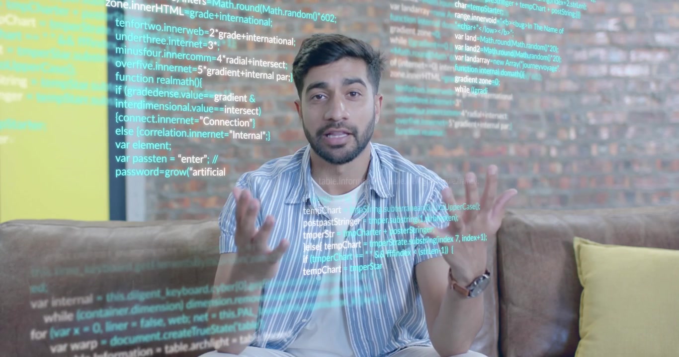 Male presenter sitting on leather couch initiating code overlay while explaining programming steps