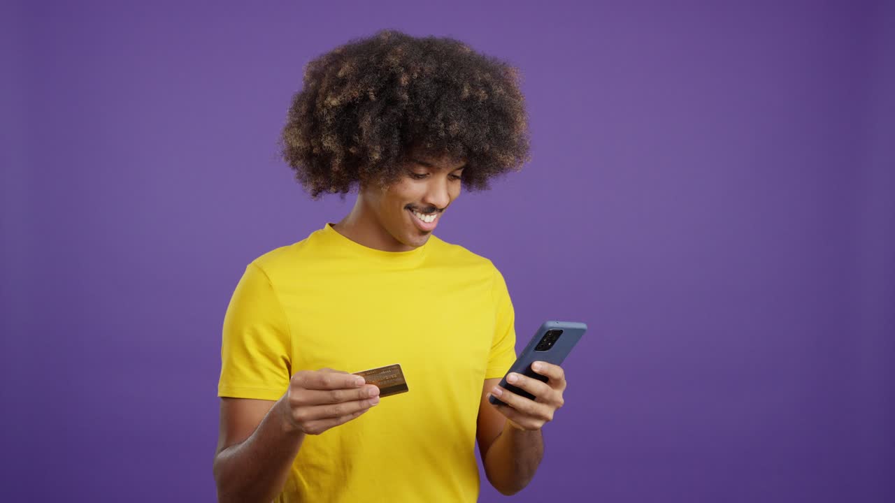 Smiling man with afro hair using a smartphone and credit card for online shopping