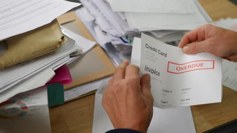 a man opening a stack of bills and letters with overdue notice for credit card debts