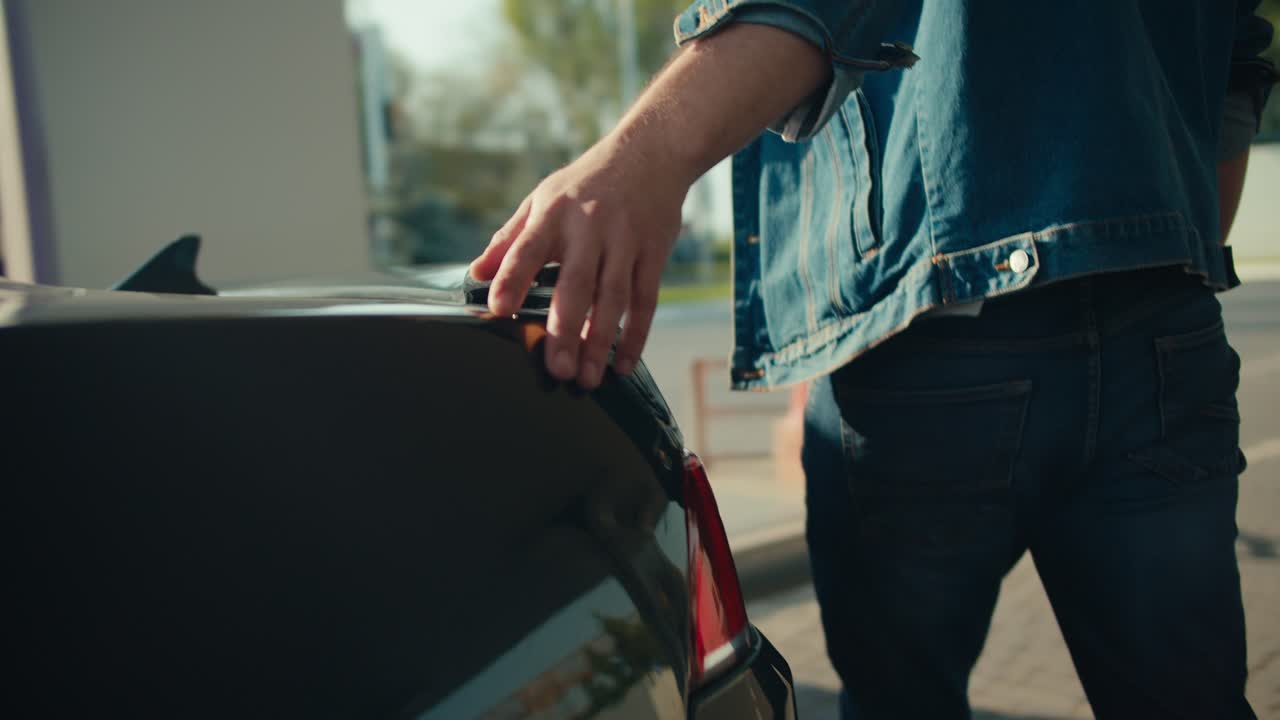 Close-up shot of a guy slamming the front door of a gray convertible and filling up his car at a gas station