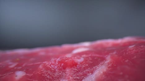 Mit-Behandschuhten-Händen-Gießt-Eine-Person-Zusatzstoffe-Auf-Fleisch,-Dreht-Es-Und-Legt-Es-Auf-Eine-Oberfläche-Mit-Kleinen-Gemüsestücken,-Was-Das-Konzept-Der-Fleischzubereitung-Und-Kulinarischen-Expertise-Veranschaulicht