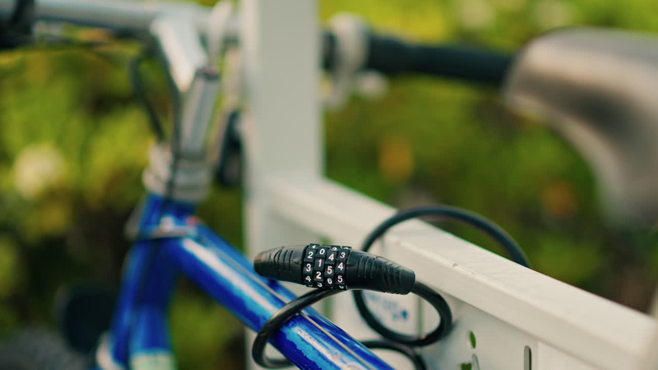 Close up of a cable lock securing a blue bike to a white fence