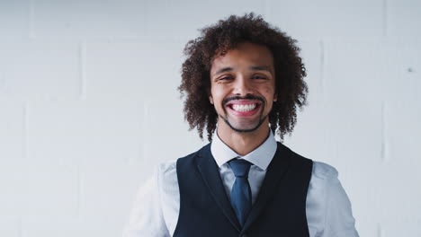 Portrait-Of-Smiling-Young-Businessman-Wearing-Suit-Standing-Against-White-Studio-Wall