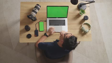 top view of asian male video editor yawning and sleeping while using green screen laptop and smartphone next to the camera in the workspace at home