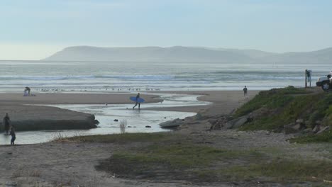 a surfer walks across an estuary along the central california coast