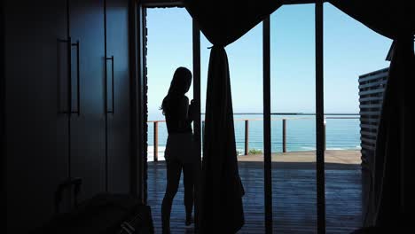 Silhouette-of-girl-leaving-room-towards-deck-overlooking-sea
