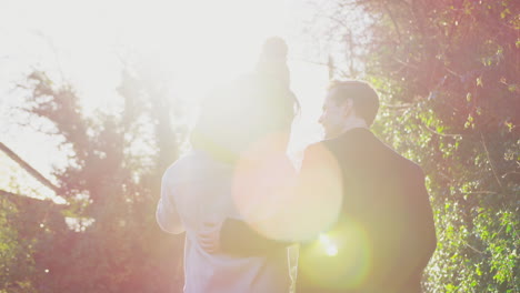 Rear-View-Of-Family-With-Two-Dads-On-Walk-In-Winter-Countryside-Carrying-Daughter-On-Shoulders