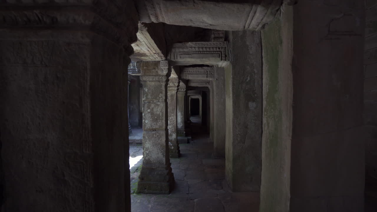 Interior hallway of Angkor temple with columns and shadows cast by soft daylight, walk through POV