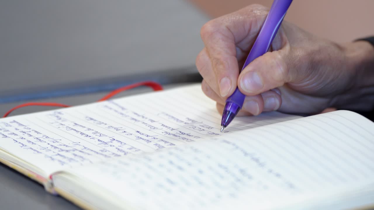 close-up shot of a person writing notes in a notebook with a blue pen