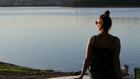 Frau-Sitzt-Bei-Sonnenuntergang-Am-Ruhigen-Wasser,-Frau-Blickt-Zur-Goldenen-Stunde-Auf-Das-Meer