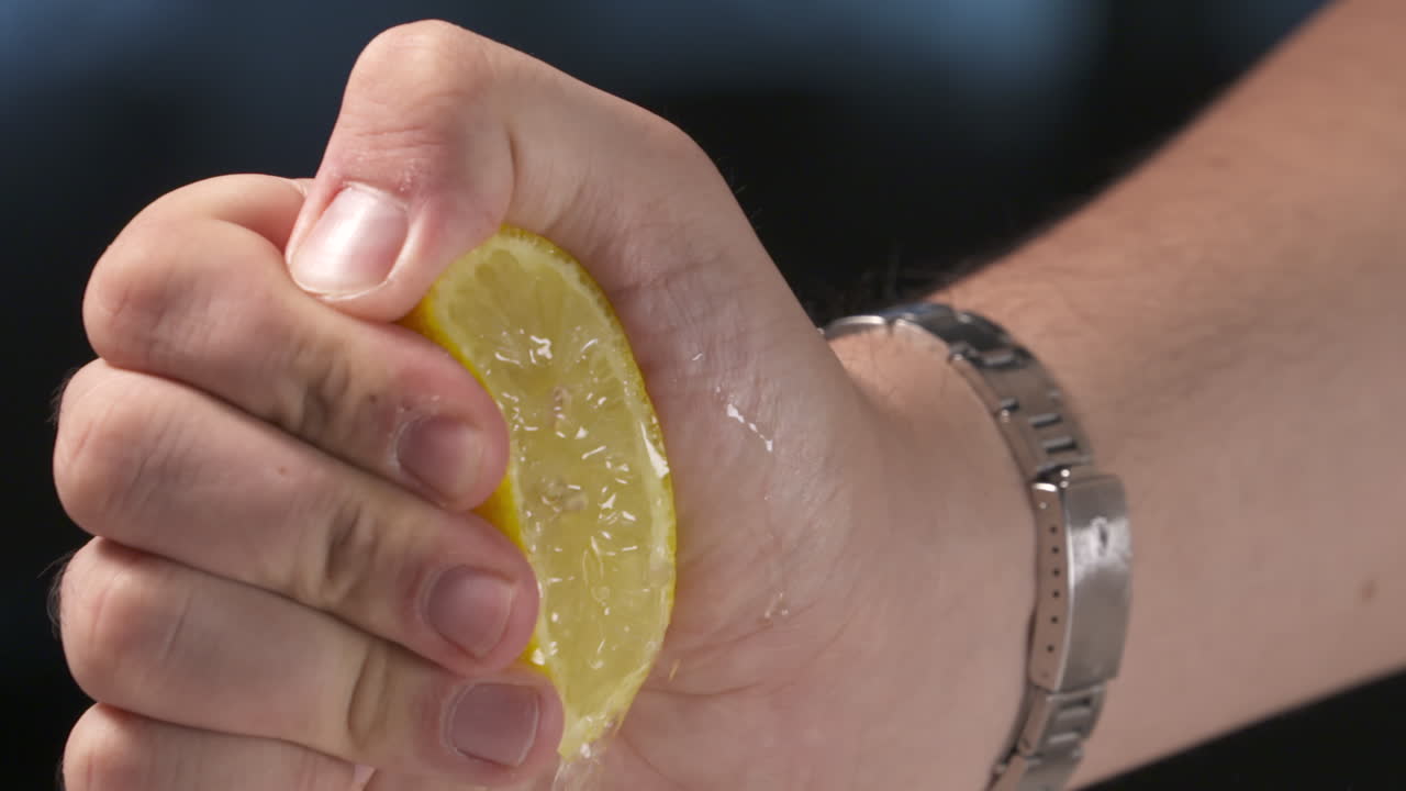 신선하고 맛있는 레몬이 손목 시계를 착용 한 남성 손에 의해 압축됩니다.