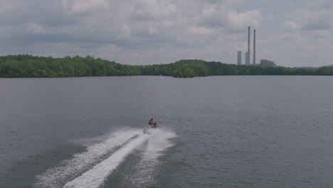 slow motion aerial footage of a jet ski on a lake with a power plant in the background