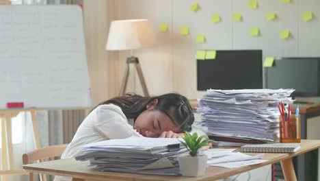 mujer asiática cansada durmiendo debido a trabajar duro con documentos en la oficina