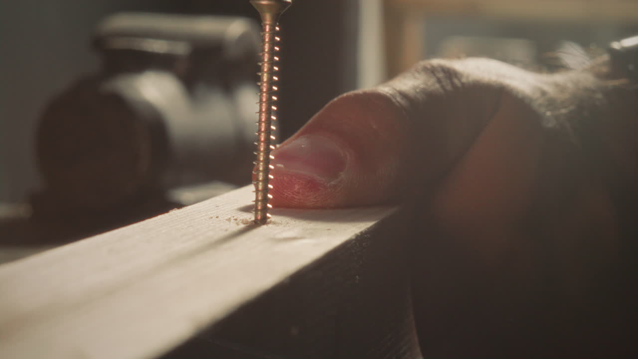 Hands of Carpenter Driving Screw into Wooden Plank with Drill