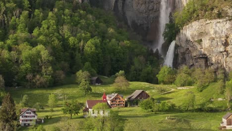 Charming-rural-scene-with-houses,-lush-greenery,-and-Seerenbach-Falls-cascading-down-a-cliff-in-Amden,-Betlis,-near-Walensee,-Switzerland