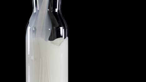 close-up of milk being poured into glass bottles against a dark backdrop, highlighting the smooth flow and clarity.