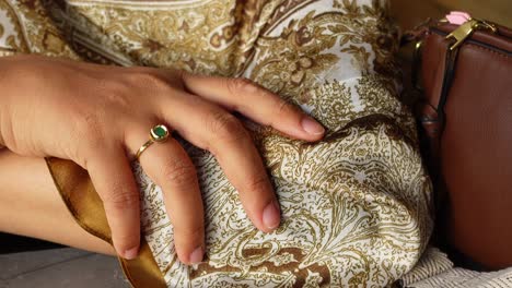 close-up of a hand wearing a gold ring with a green emerald gemstone