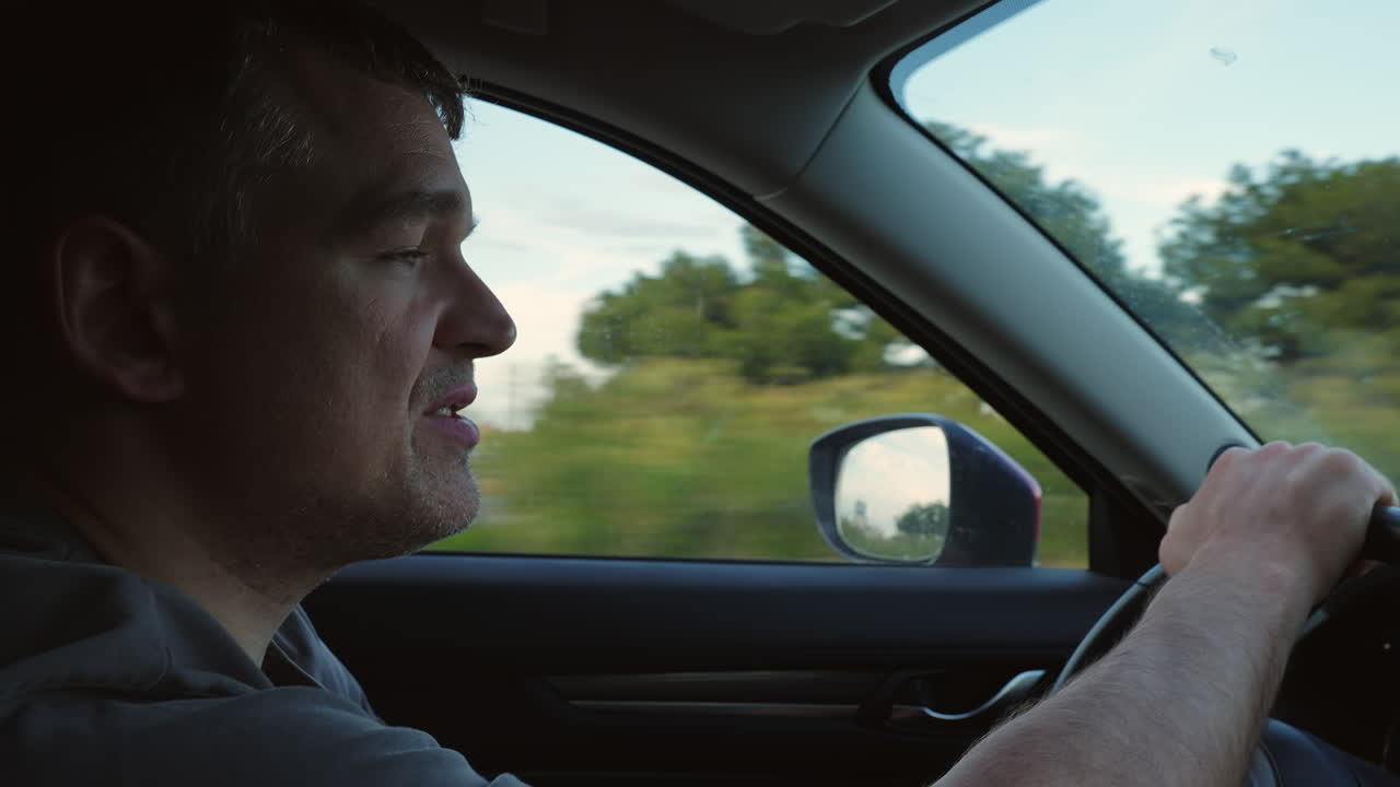 Voksen mann kjører bil og snakker mens han kjører.