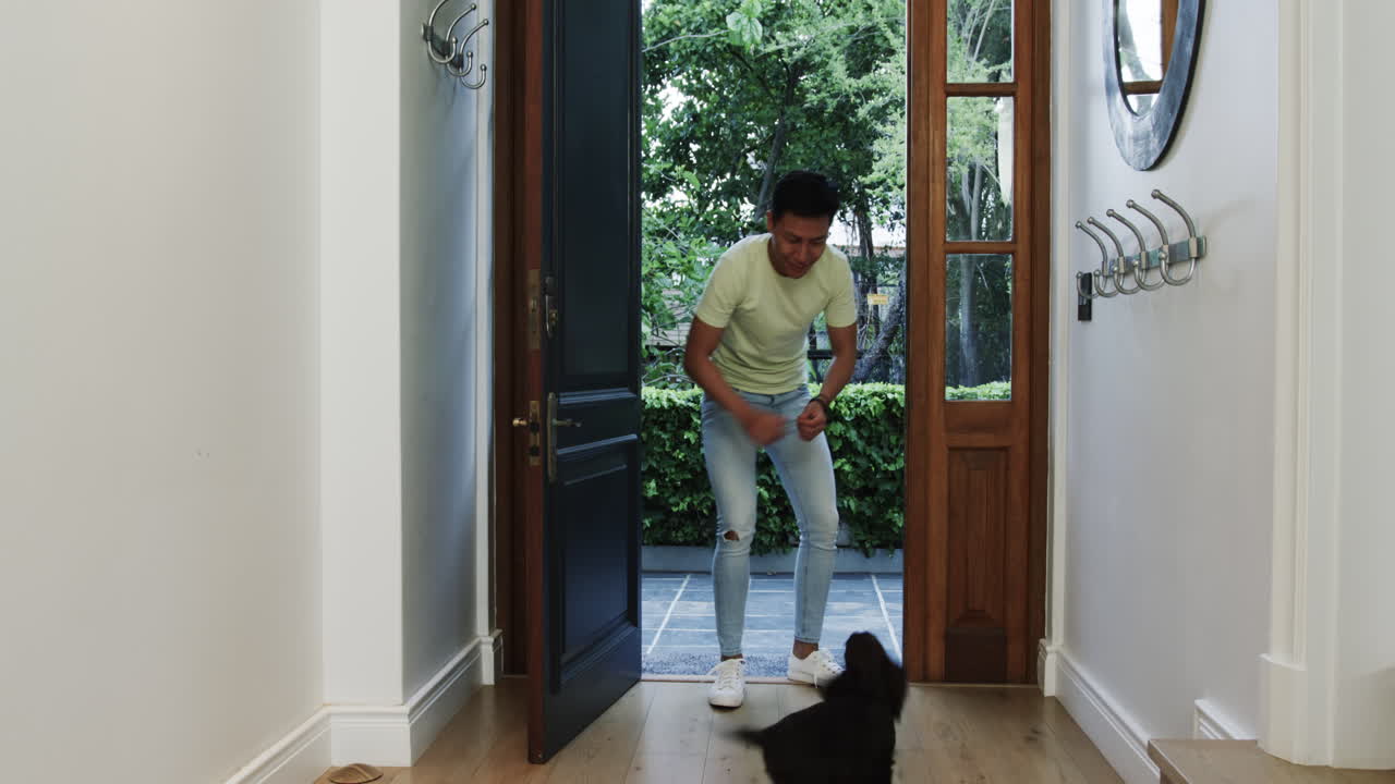 Asian man playing with small dog at home entrance, enjoying quality time
