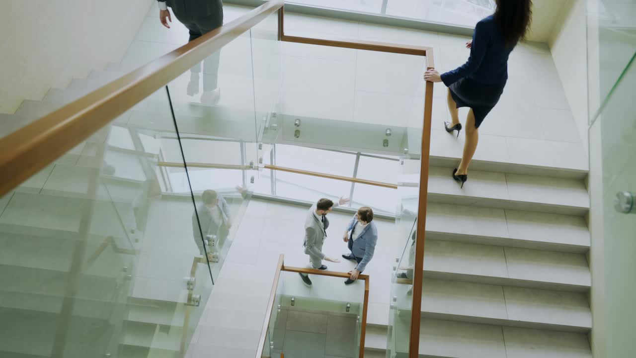 vista superior de dos hombres de negocios se reúnen en la escalera en el centro de oficinas modernas y hablando mientras las colegas femeninas caminan por las escaleras