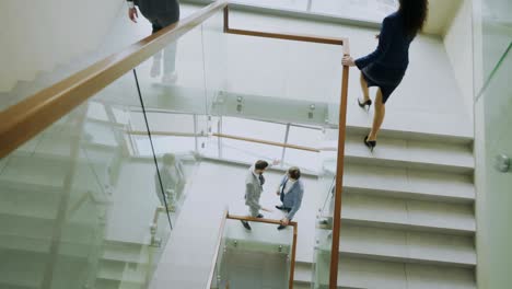 top view of two businessmen meet at staircase in modern office center and talking while female colleagues walking stairs