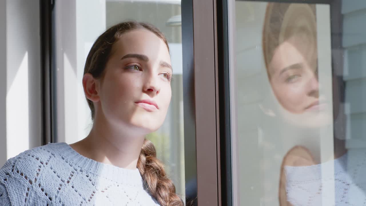 mujer caucásica pensativa sonriendo y mirando a través de la ventana en cámara lenta