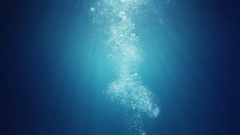 Underwater-sunlight-beams-shining-from-above-coming-through-the-deep-crystal-clear-blue-water-causing-a-beautiful-water-lighting-reflections-curtain-with-air-bubbles-rising-up-to-the-surface