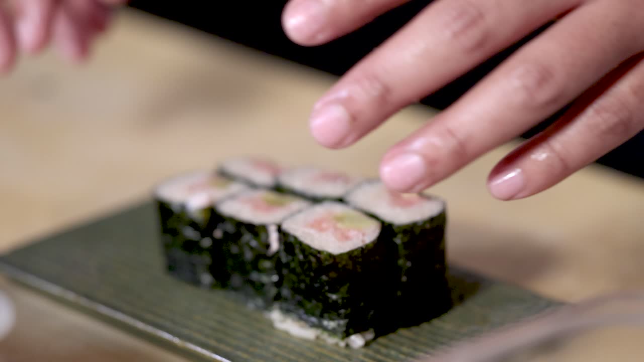 Primo piano di mani che dispongono maki sushi freschi su un piatto di ceramica verde текстуrаto