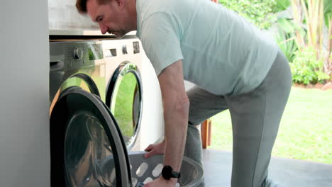 senior man doing laundry at home, loading washing machine with clothes