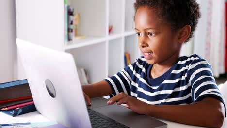 young boy sitting at desk in bedroom using laptop computer
