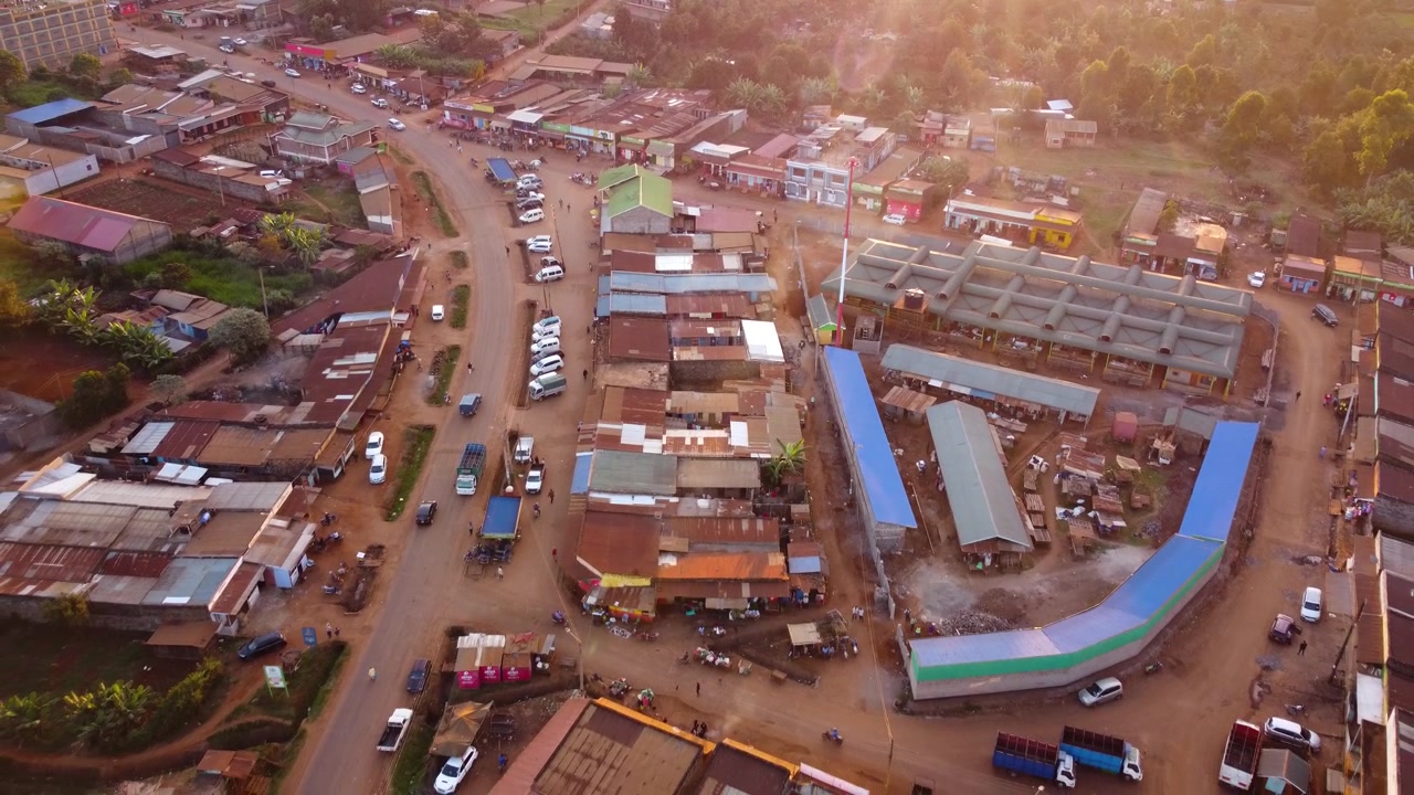 Vista aerea di un vivace mercato rurale a Embu, Kenya, illuminato da una calda luce serale, che mostra negozi, strade, attività commerciali, veicoli e attività commerciale in una comunità agricola.