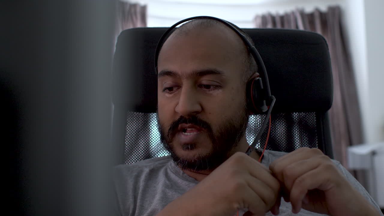 un hombre calvo serio y enfocado que usa audífonos sentado en una computadora portátil moderna en la oficina en casa, discutiendo el trabajo en el teletrabajo en línea