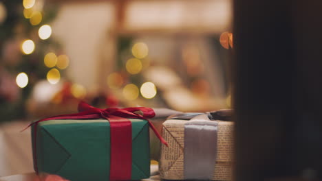 Beautiful-gift-in-the-hands-of-men.-New-Year's-gift-with-a-red-ribbon,-fir-on-the-table.-The-man-made-it-himself-and-is-going-to-give-for-the-holiday.-Beautiful-background-with-fireplace.