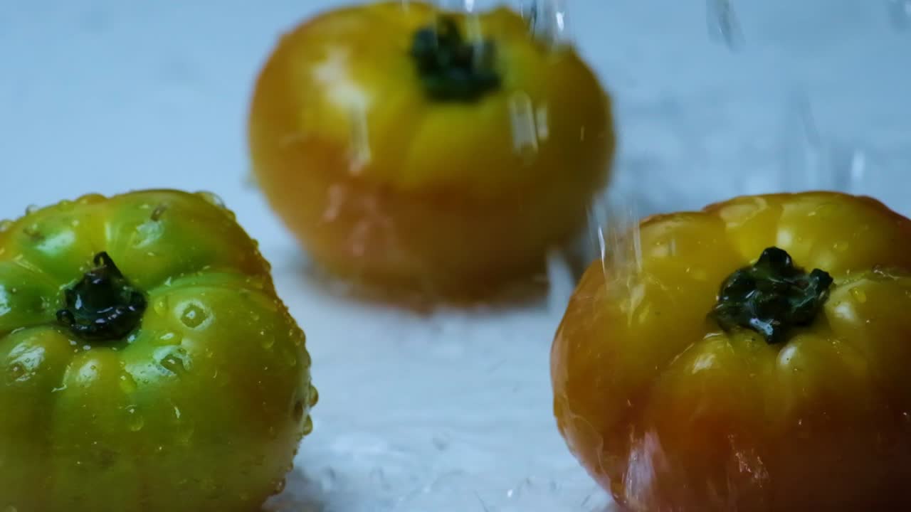 gotas de agua salpican bajando sobre tres grandes tomates de carne de res en una superficie blanca