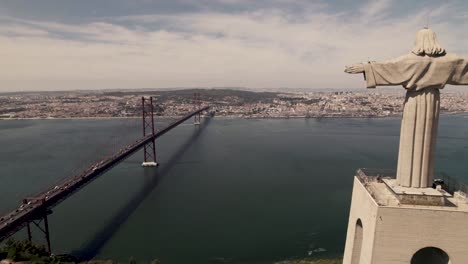 aerial pull out shot overlooking at lisbon capital city, reveals clifftop statue of cristo rei in almada