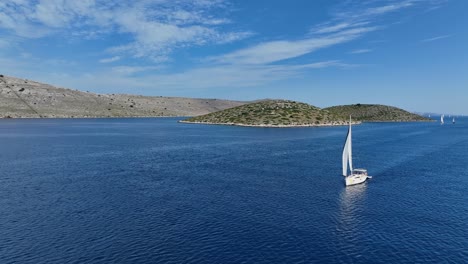 lone sailboat drifts across deep blue waters with distant islands in kornati, croatia, aerial frontal orbit under blue sky
