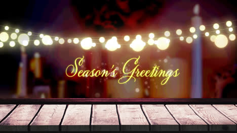 Seasons-greetings-text-and-glowing-yellow-fairy-light-decoration-hanging-over-wooden-plank