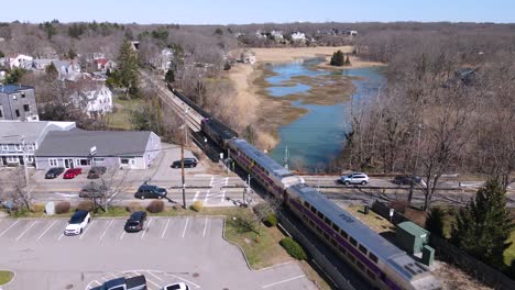 train on its tracks through small village diagonally next to marsh with stopped cross traffic, static drone shot