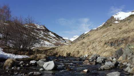 Idyllic-mountain-landscape-in-the-Pyrenees-National-Park--Drone-flies-slowly-over-a-mountain-stream-with-the-snowy-peaks-of-the-Pyrenees-in-the-background