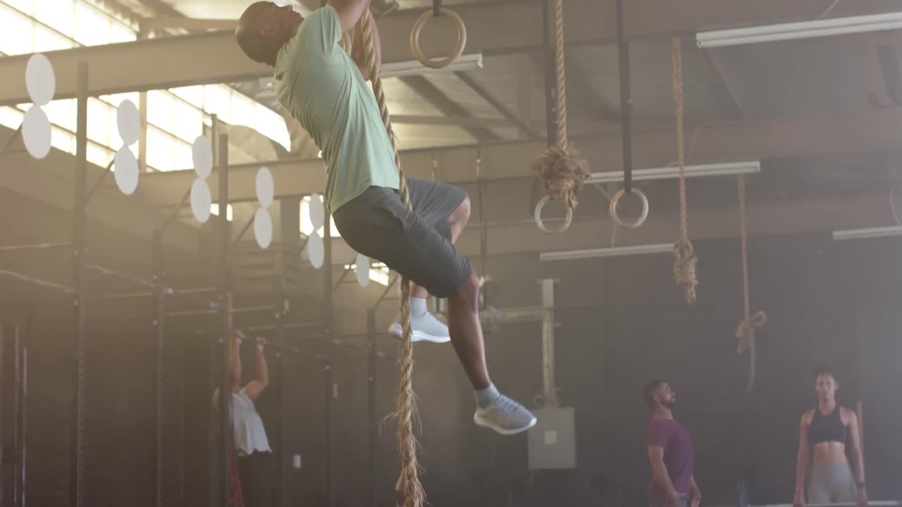 Uomo birazziale che si allena in palestra arrampicandosi sulla corda, al rallentatore.